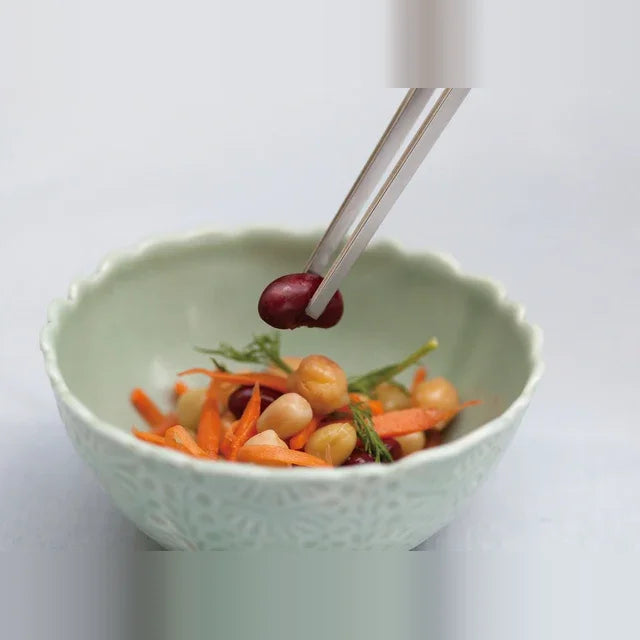 Saibashi tongs picking up a bean from a bowl of vegetables