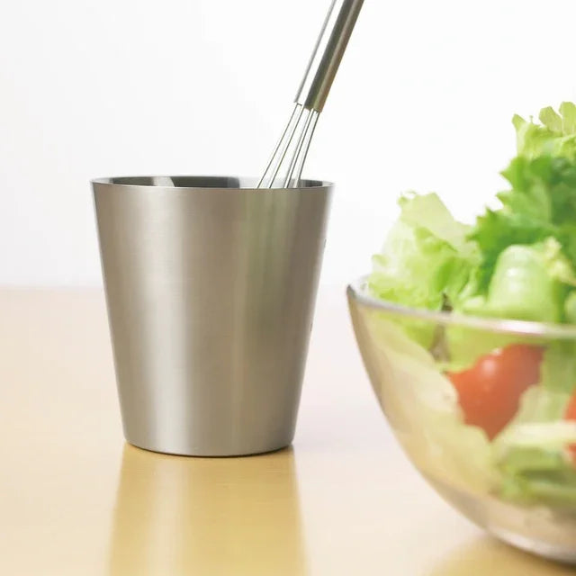Mazelu whisk in a stainless tumbler next to a salad