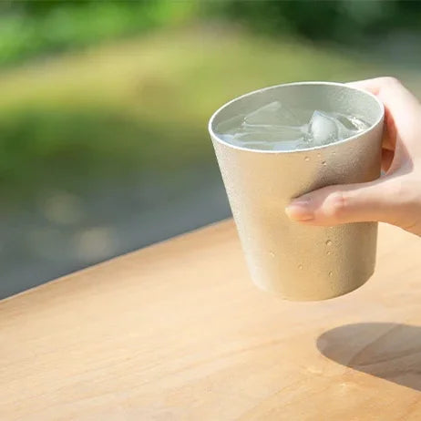 Hand holding a NAJIMI tin tumbler outdoors