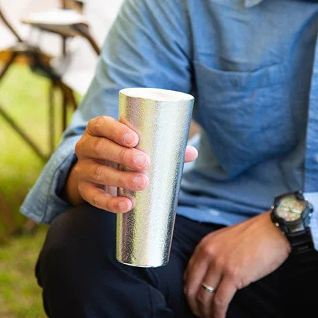Man holding a tin beer cup outdoors
