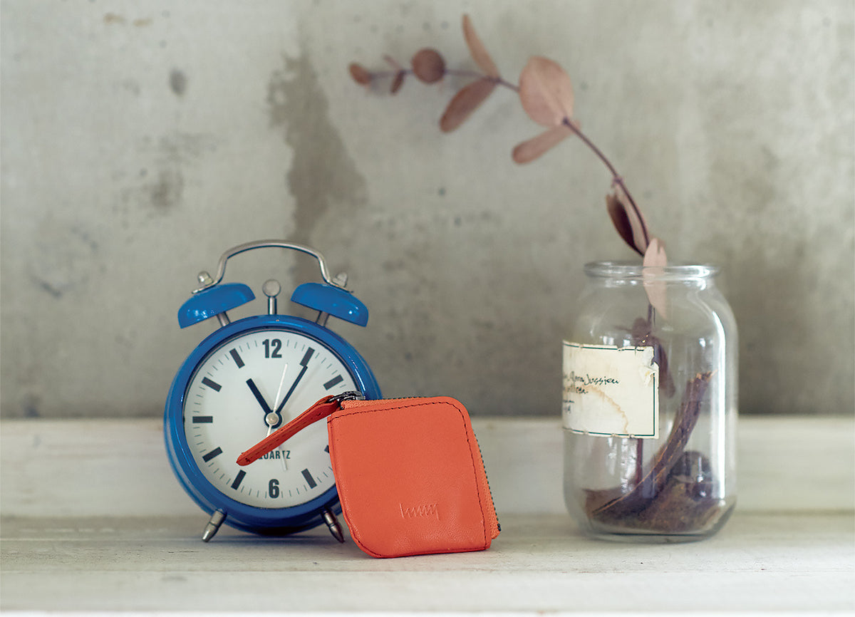Orange hmny mini coin purse beside a clock