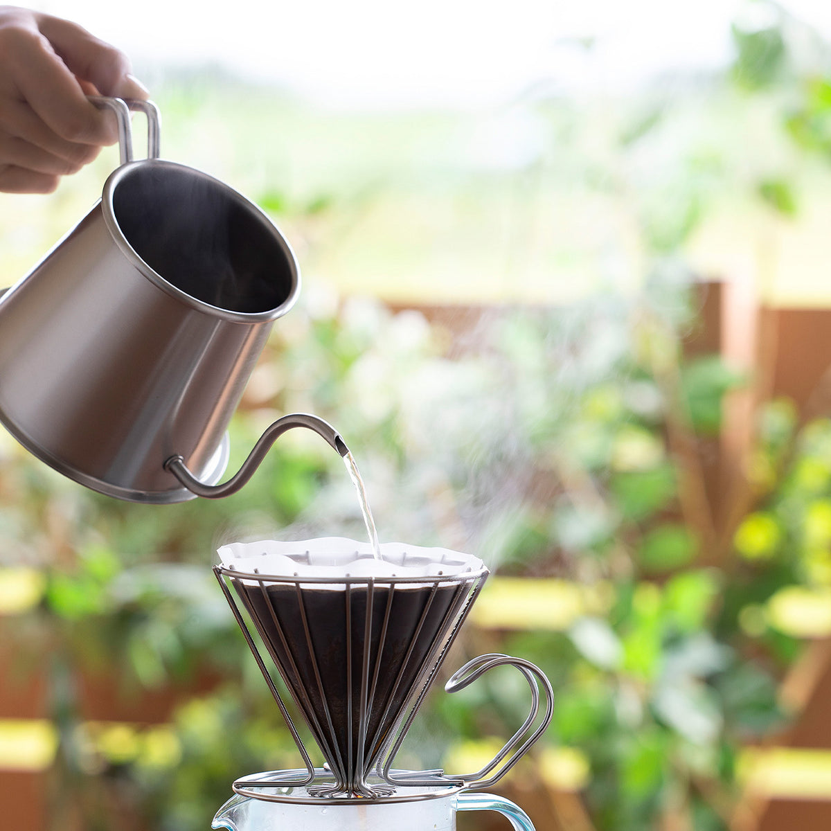 Pouring hot water from the Two Drip Pot Pro into a dripper outdoors