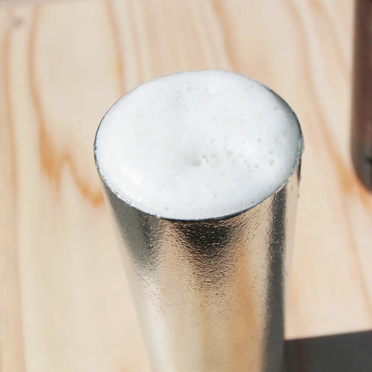 Close-up of fine, creamy beer foam in a tin beer cup