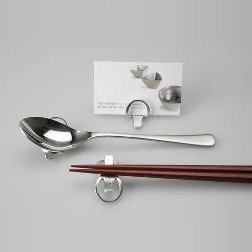 Tin chopstick rests bent to hold a spoon, chopsticks and a card